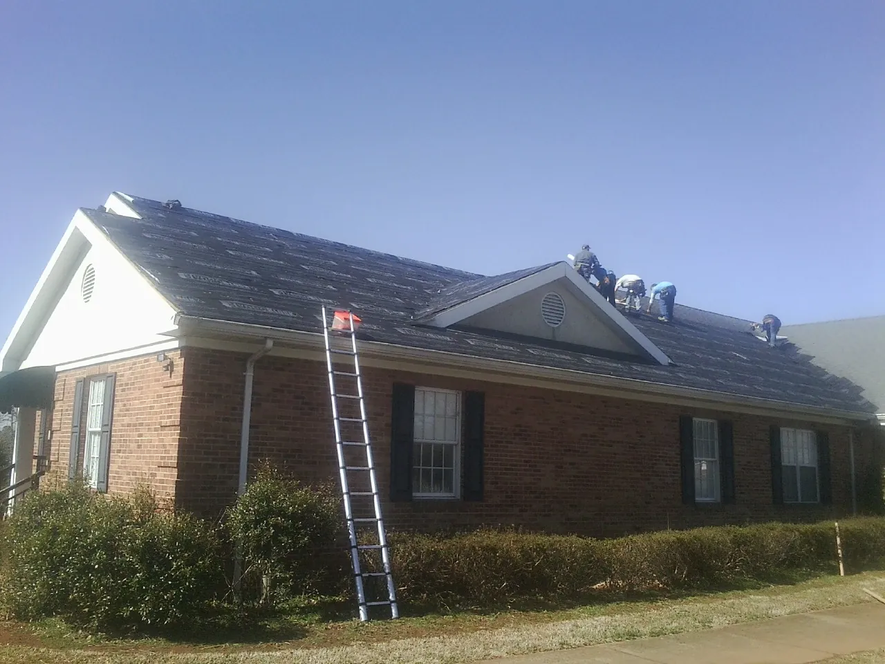 Crew tearing shingles off a brick ranch roof with a ladder set — Emergency Roof Repair work by our crew in Bonifay