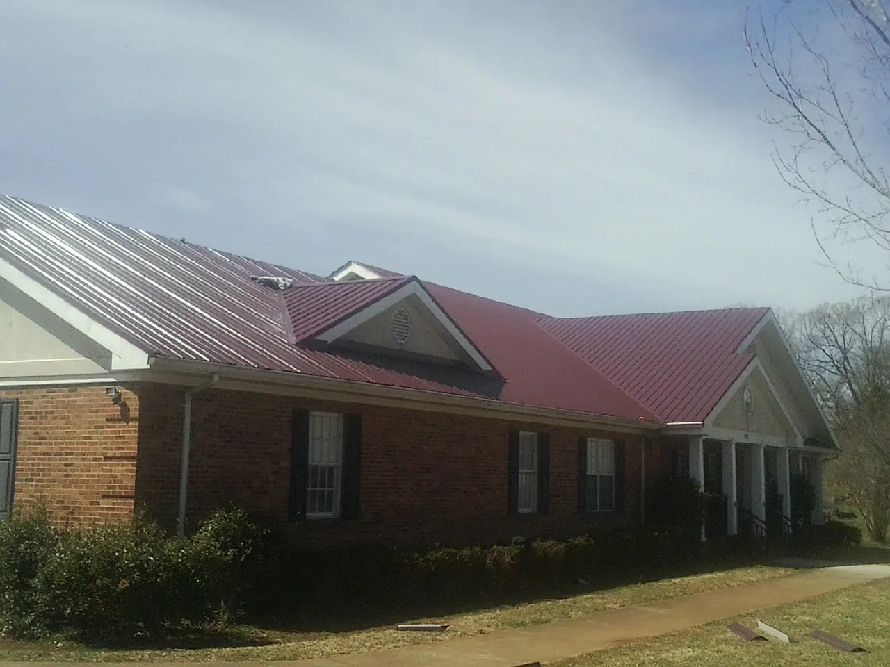 Red metal roof with gabled entries on a long brick building, from a Hail Damage Roof Repair job in Bonifay