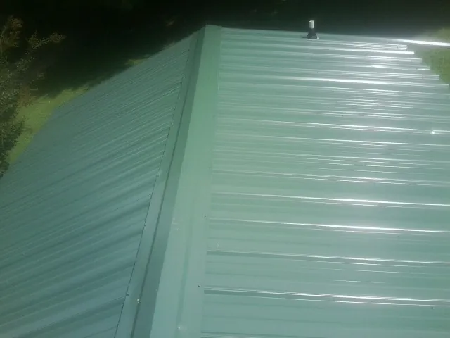 New green metal panels meeting at the ridge of a roof — Flat Roof Repair work by our crew in Bonifay