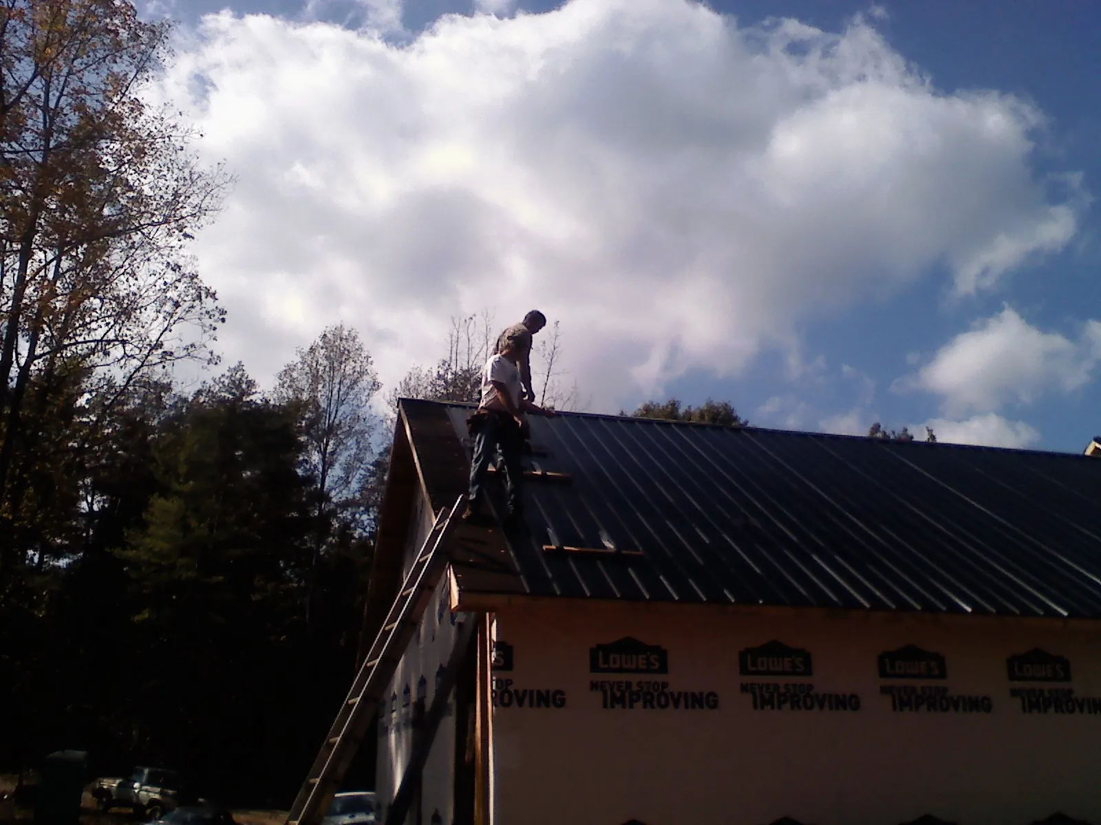 Roofer fastening dark metal panels high against a cloudy sky, from a Roof Inspection job in Bonifay