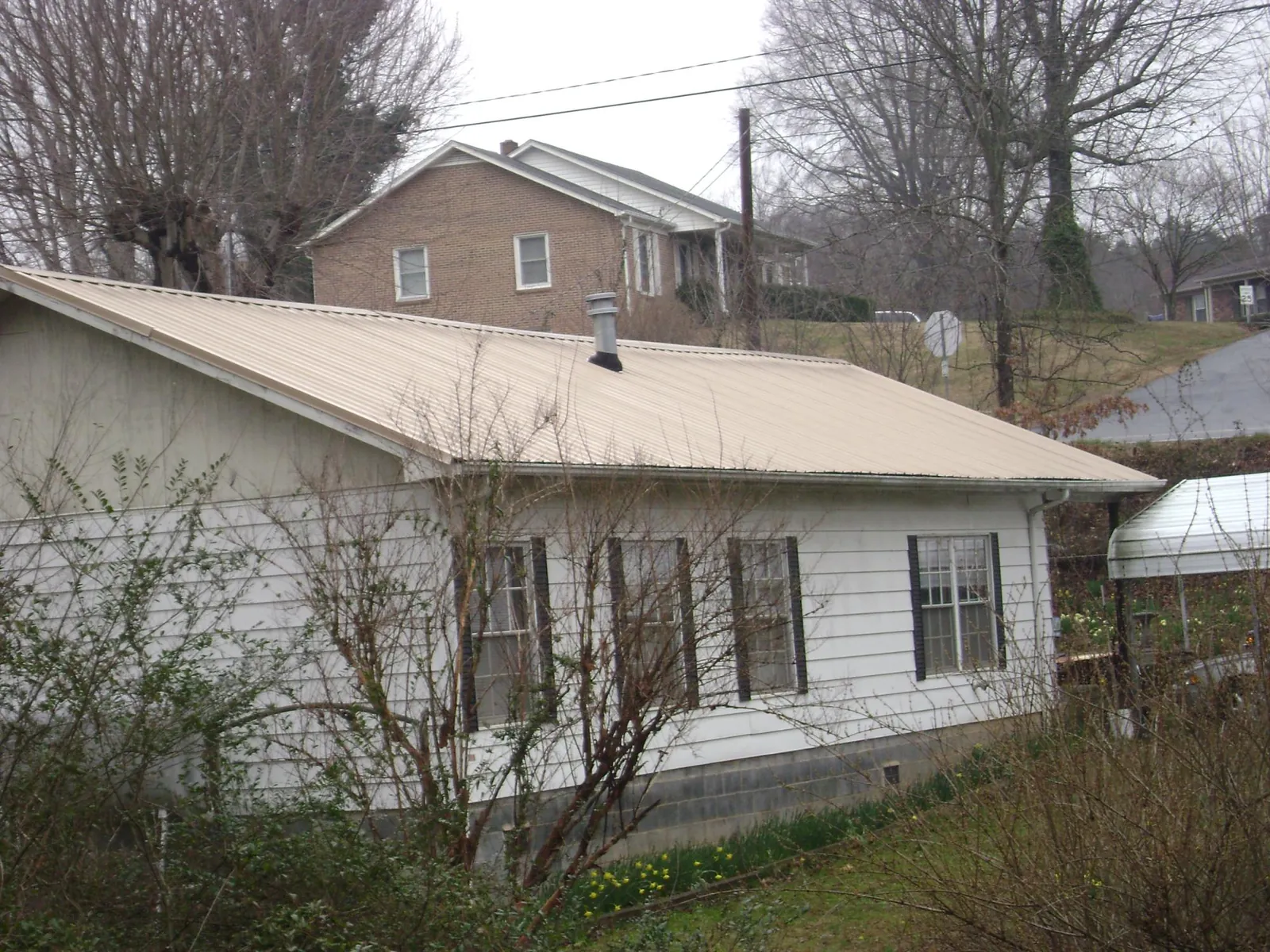 Tan metal roof on a white sided house set into a hillside — Commercial Roofing by Roofing Brothers in Bonifay