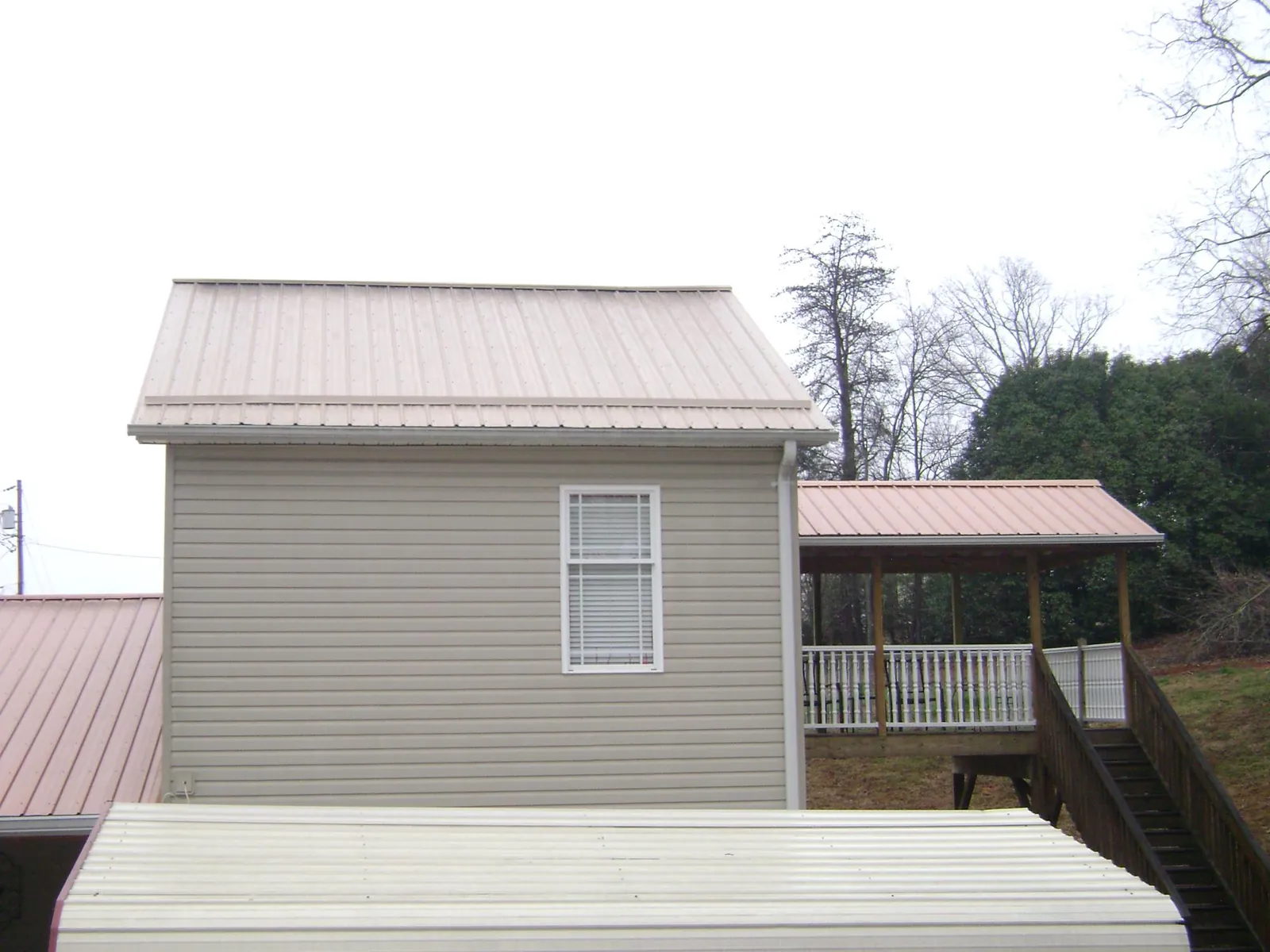 Tan metal roofs on a two story addition and attached porch, from a Roof Replacement job in Bonifay